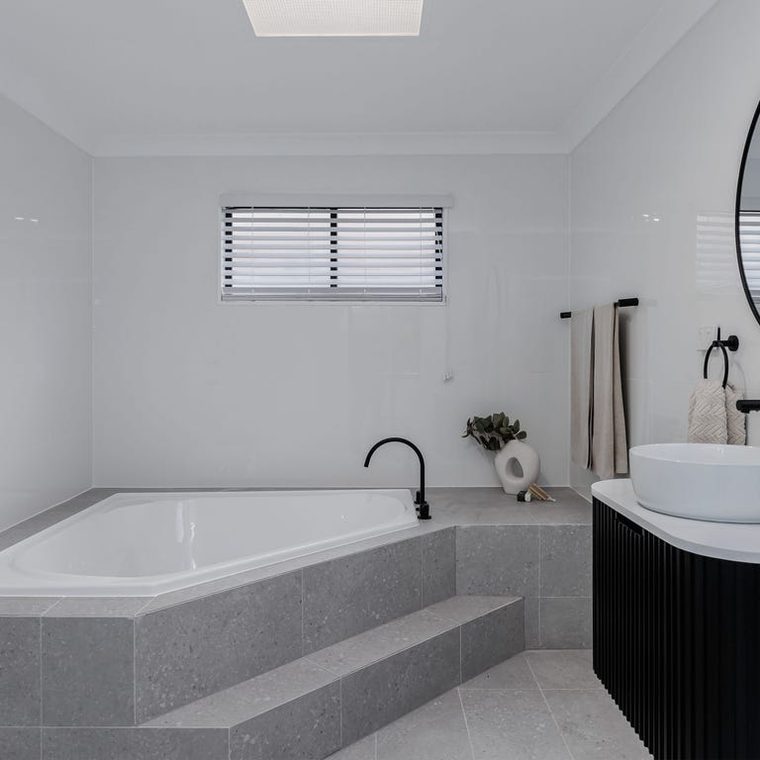 Bathroom after — white tiling, black tapware and a round mirror