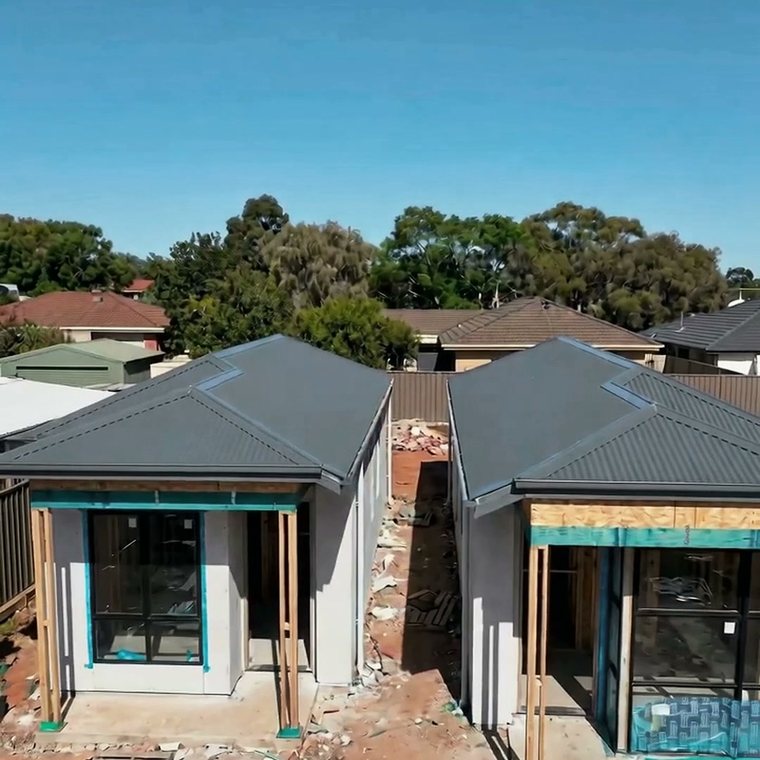The same block today — two homes framed with roofs on and render started
